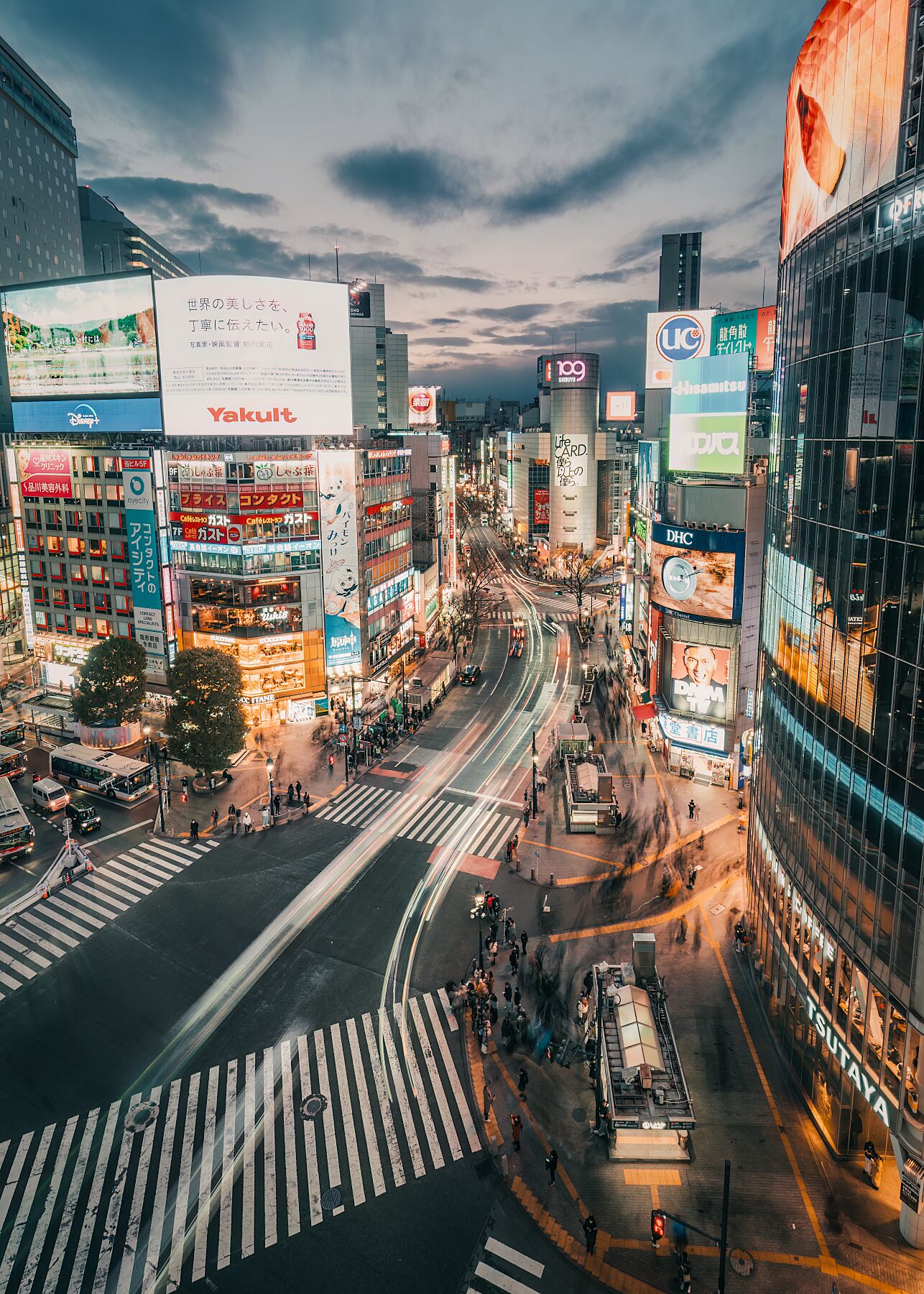 A high-angle view of Shibuya Crossing, Tokyo, with light trails from passing cars.